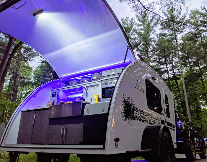 RV rental: A Luna Rover teardrop trailer's outdoor kitchen, lit with vibrant purple LEDs, open for camping in pine woods. — photo 13