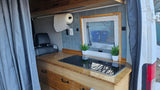 Compact RV rental interior featuring a bamboo kitchen counter with cooktop, window, and storage.