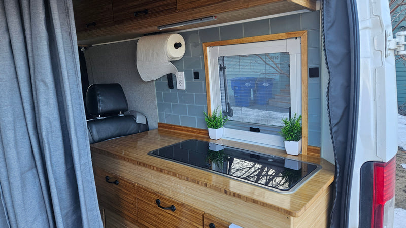 Compact RV rental interior featuring a bamboo kitchen counter with cooktop, window, and storage. — photo 2