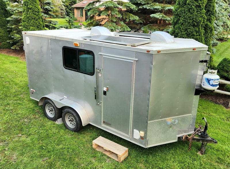  parked on grass.|A light gray enclosed cargo trailer with dual axles and rear doors — photo 5