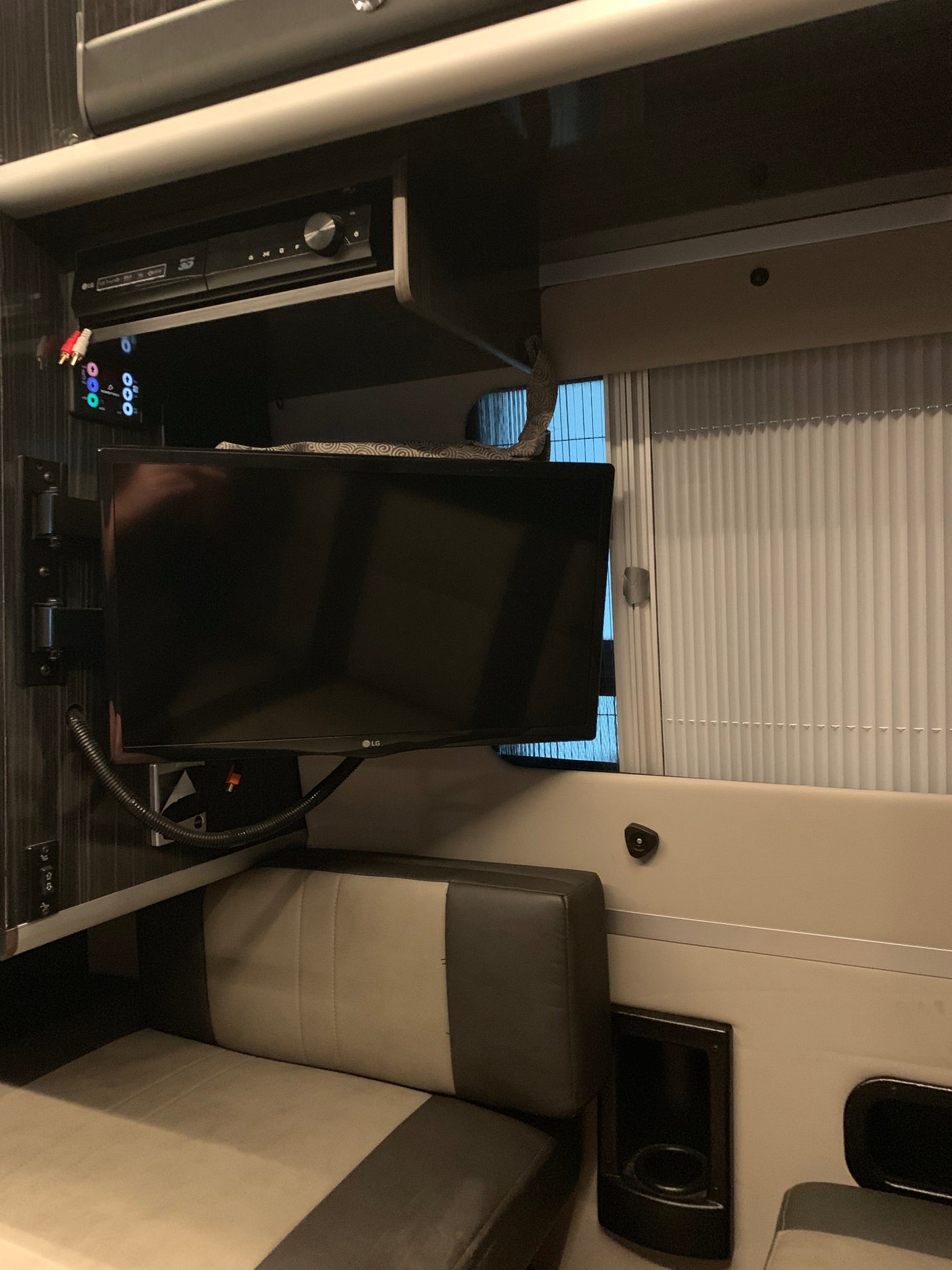 Inside an RV rental: a compact living area with TV, entertainment system, and comfortable seating with cupholders.