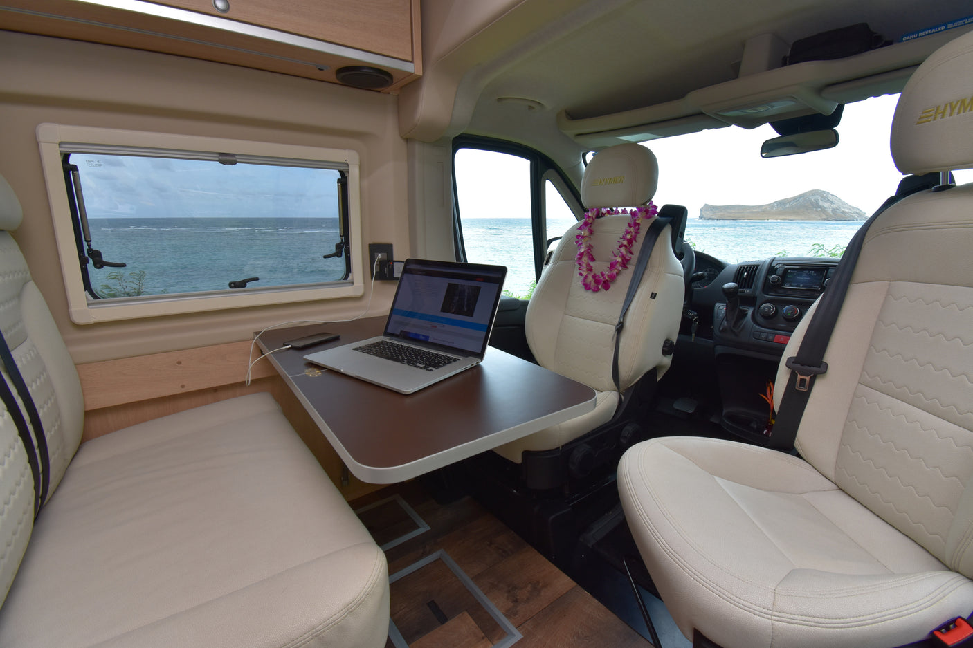 Remote work from your RV rental: a comfy interior with laptop, ocean, and island views, plus a welcoming lei.