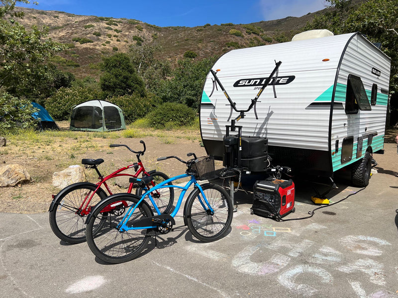 RV rental parked at a sunny mountain campsite with bikes, tents, and a generator on pavement with kids' chalk art. — photo 3
