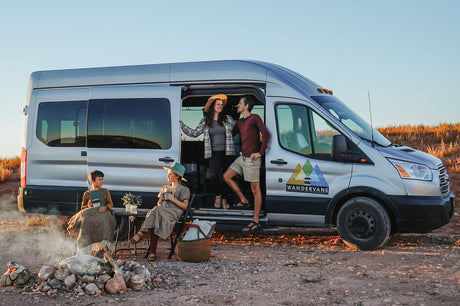 Family enjoying a campfire beside their silver Ford Transit rv rental van. Adults stand by the open door, kids sit near the fire.