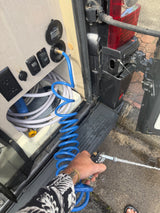 Cleaning outside an **rv rental**: A person sprays water from a coiled hose connected to the van's external utility panel and water pump.