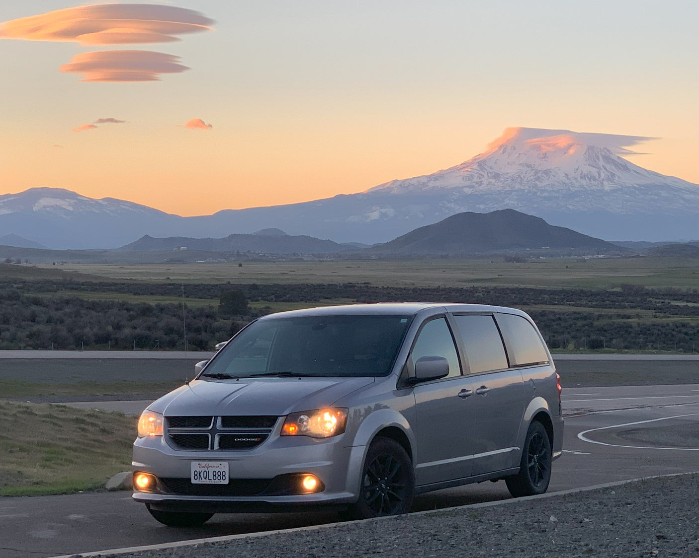 Travel van parked at sunset with unique lenticular clouds over snowy mountains. Planning an RV rental getaway?