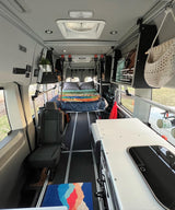 Organized camper van interior with cozy bed, passenger seat, & custom kitchenette. Ready for your next rv rental road trip!