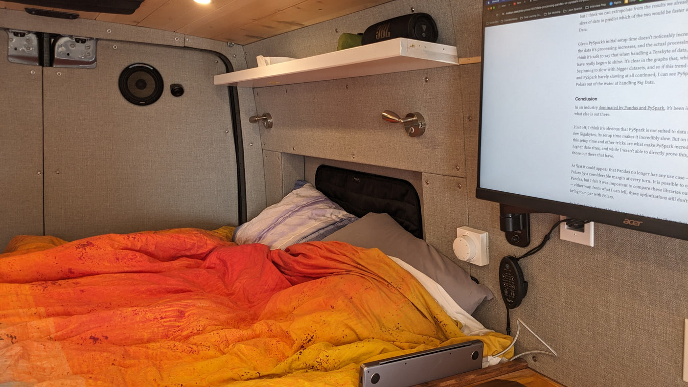 RV rental bedroom, vibrant bedding. Monitor shows data processing article (PySpark, Pandas, Polars comparison).