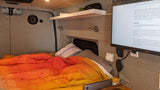 RV rental bedroom, vibrant bedding. Monitor shows data processing article (PySpark, Pandas, Polars comparison).