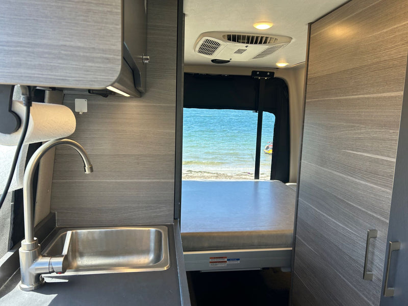  and a small window with blinds.|RV rental adventure: Camper van with bikes parked amidst majestic mountains and pine trees under a clear blue sky.|Camper van (RV rental) and bikes parked at iconic Monument Valley for desert adventure.|Camper van RV rental: Interior shows front seat — photo 10