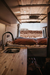 Cozy RV rental interior with a kitchen, offering stunning desert views right from the comfortable bed.