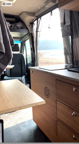 RV rental interior with a bright beach view, showing a compact kitchen, pull-out table, and integrated storage.