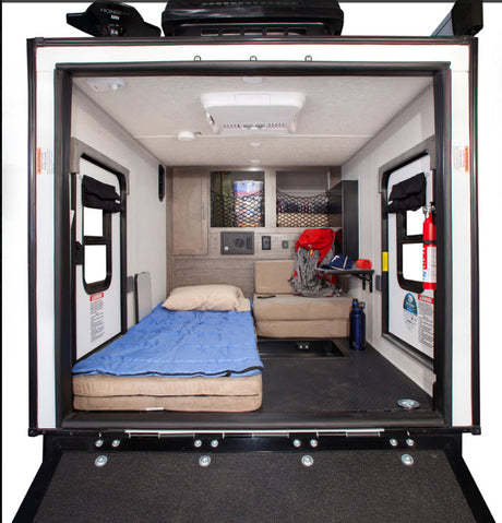 Spacious RV rental interior: A toy hauler's versatile living/garage area with bed, sofa, storage, and ramp. Perfect for adventures.