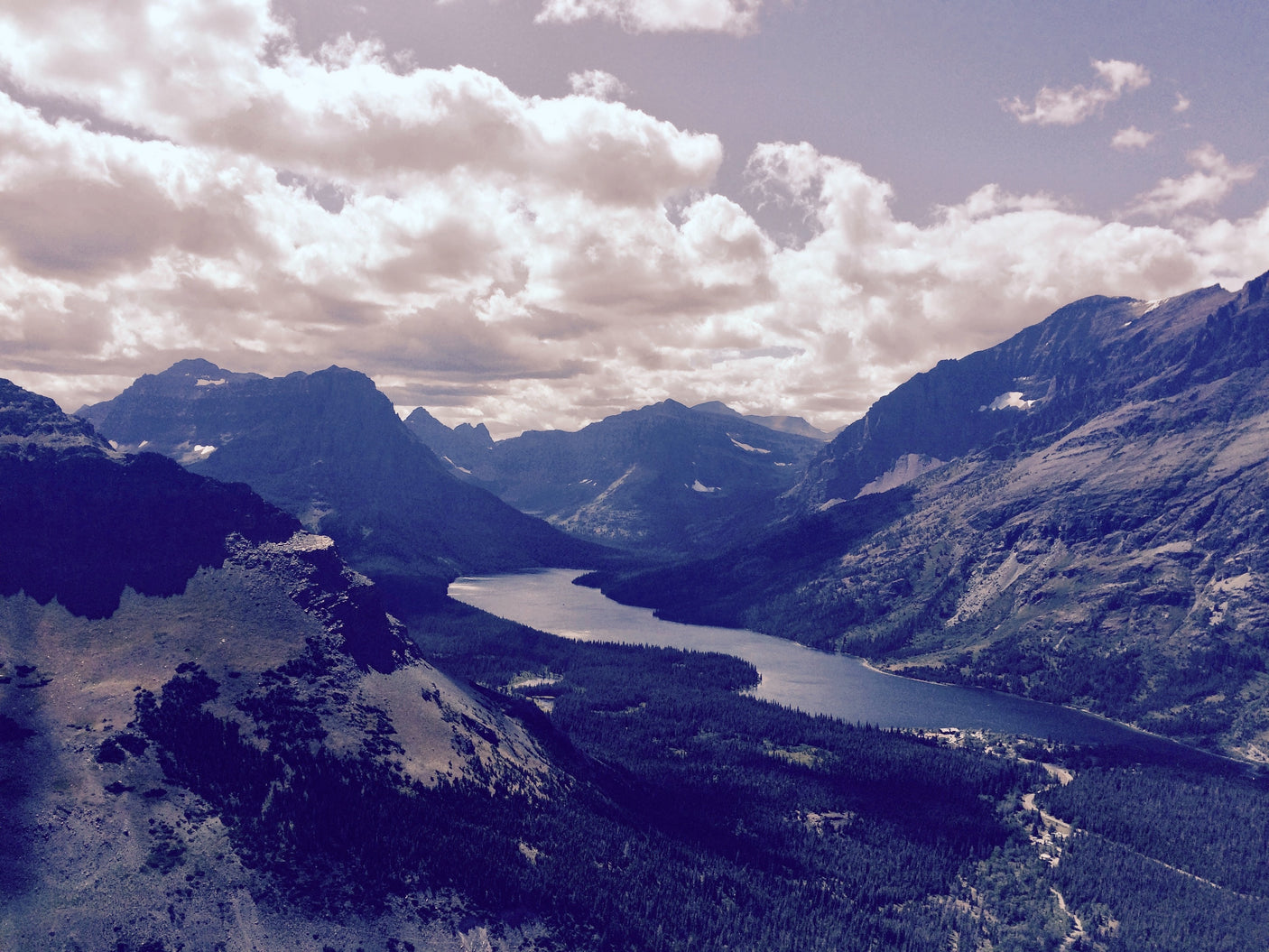 Panoramic view from above a winding mountain lake, forests, and peaks in Glacier National Park; ideal for an RV rental.
