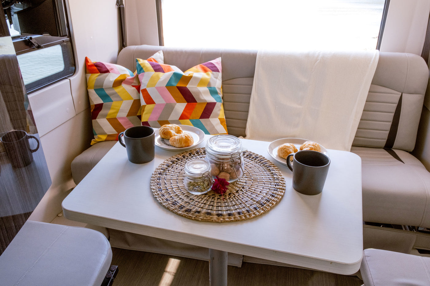 Cozy RV rental interior with breakfast setup: mugs, croissants, and colorful pillows on a light-colored table. — photo 6