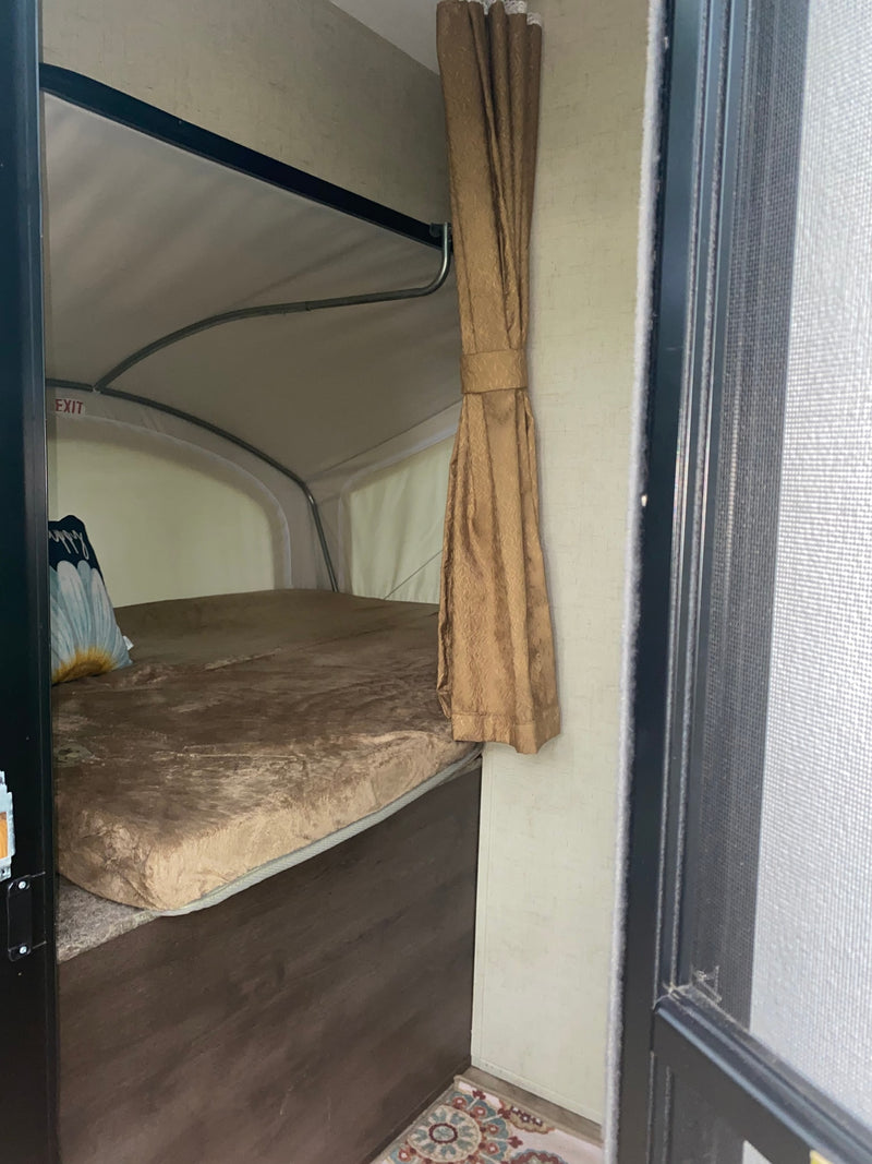 Inside an RV rental pop-up camper, showing the bed, soft mattress, and cozy interior space with a curtain and exit sign. — photo 9