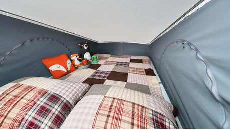Cozy pop-top sleeping area in an RV rental, featuring patchwork bedding, pillows, and cute stuffed animals for adventure.