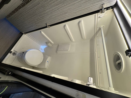 An RV rental compact wet bath with toilet, shower, drain, and molded interior walls for efficient travel.
