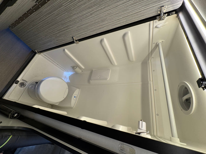An RV rental compact wet bath with toilet, shower, drain, and molded interior walls for efficient travel.