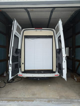White RV rental van with open rear doors, showing interior pleated blinds and storage. Parked in a garage, ready for adventures.