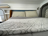 Cozy RV rental interior: A comfy bed with striped pillows, adjacent to a functional kitchen sink & shiplap walls.
