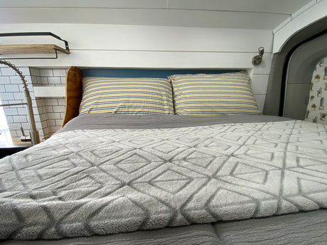 Cozy RV rental interior: A comfy bed with striped pillows, adjacent to a functional kitchen sink & shiplap walls.