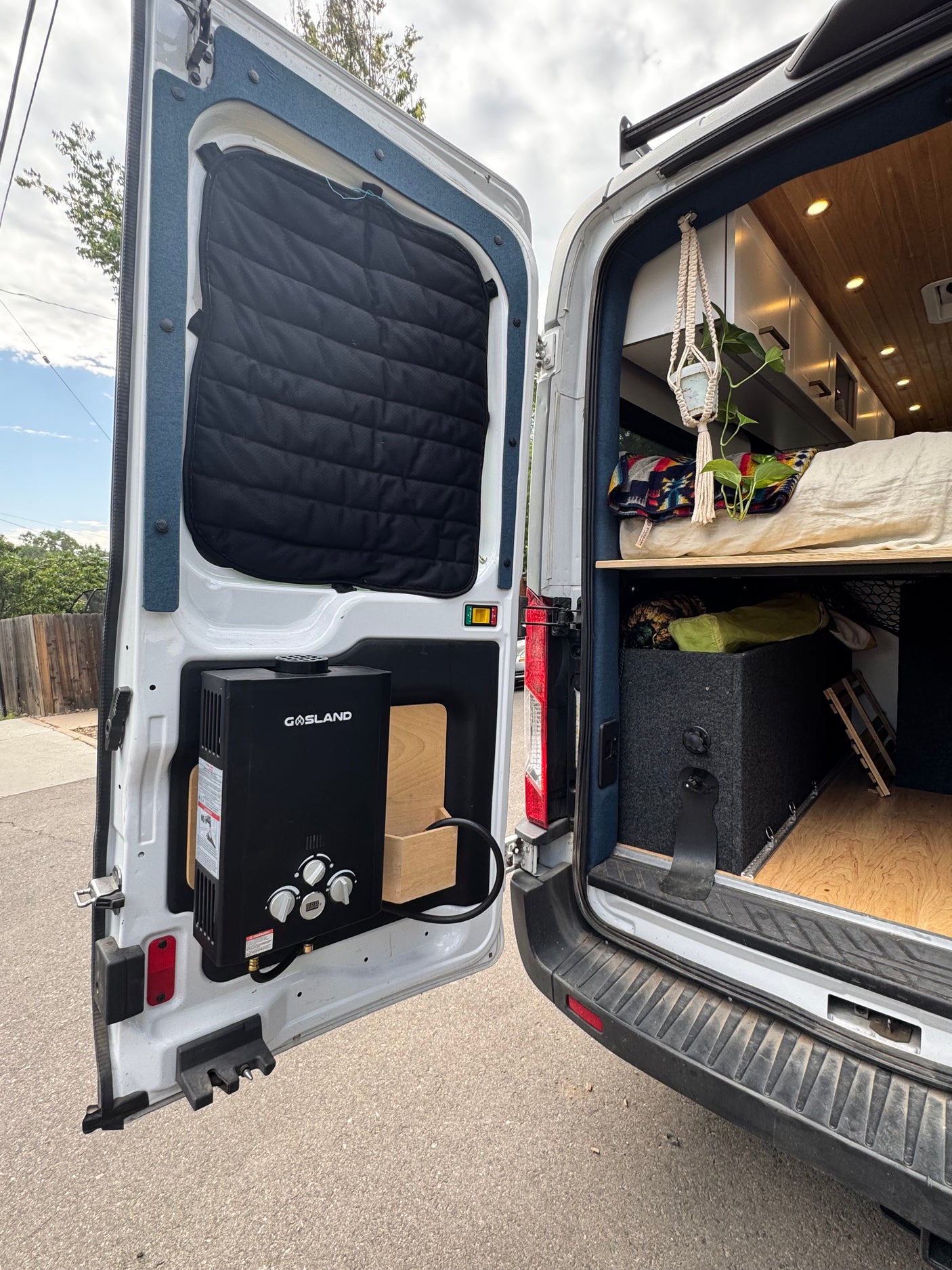 Inside an RV rental: a customized camper van with an outdoor water heater, cozy bed, and storage solutions.