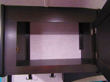Interior view of an open dark wood cabinet with pink textured lining and hooks, ideal for storage in an RV rental.