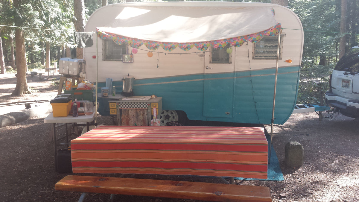 Vintage RV rental with an extended awning, picnic table, and outdoor kitchen setup at a shady forest campground. — photo 6