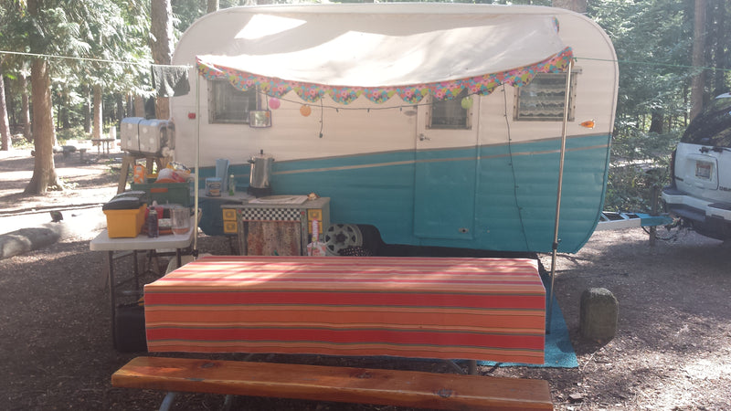 Vintage RV rental with an extended awning, picnic table, and outdoor kitchen setup at a shady forest campground. — photo 6