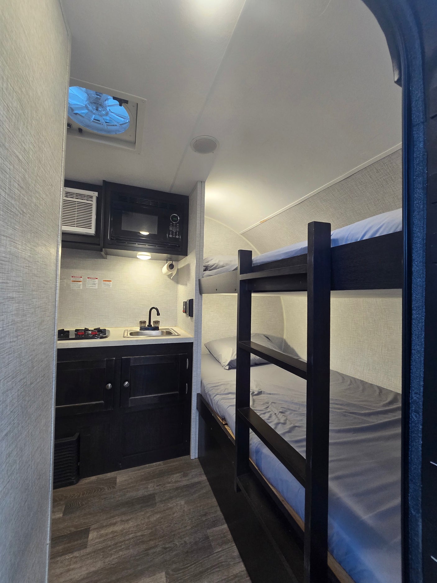 This RV rental features a compact kitchen with a microwave, sink, and stovetop, plus comfy bunk beds and a ceiling fan.
