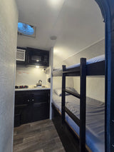 This RV rental features a compact kitchen with a microwave, sink, and stovetop, plus comfy bunk beds and a ceiling fan.
