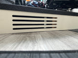 Up-close RV rental interior: white panel with climate control vents, black textured step, and wood-look floor.