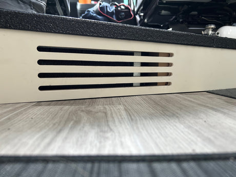 Up-close RV rental interior: white panel with climate control vents, black textured step, and wood-look floor.