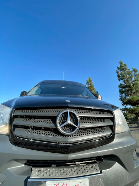 A black Mercedes-Benz Sprinter van, front-facing. Ready for an RV rental or road trip under a clear blue sky.