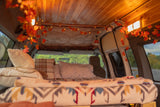 Experience cozy van life with this RV rental! Interior features autumn leaf lights, a wooden ceiling, and a comfy bed with blankets.