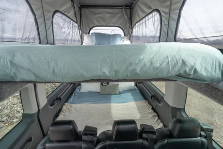 View inside an rv rental: an elevated bed and a lower bed with light blue and beige bedding, offering cozy sleeping options.