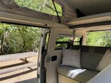 RV rental interior view: an open pop-top roof, comfy seating, and a picnic table outside in nature. Perfect for camper adventures.