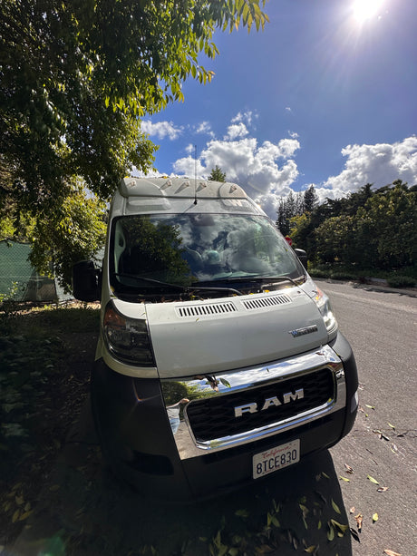 Bright Winnebago Ram ProMaster rv rental van parked under a tree on a sunny, cloudy day. Reflections in chrome grill, CA plate.