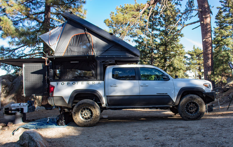 White Toyota Tacoma overlanding truck with an RV rental-style rooftop tent & camper, parked in a forest campsite. — photo 10