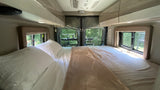 Cozy RV rental interior: a comfy bed with soft linens, windows offering natural views, and charming string lights.