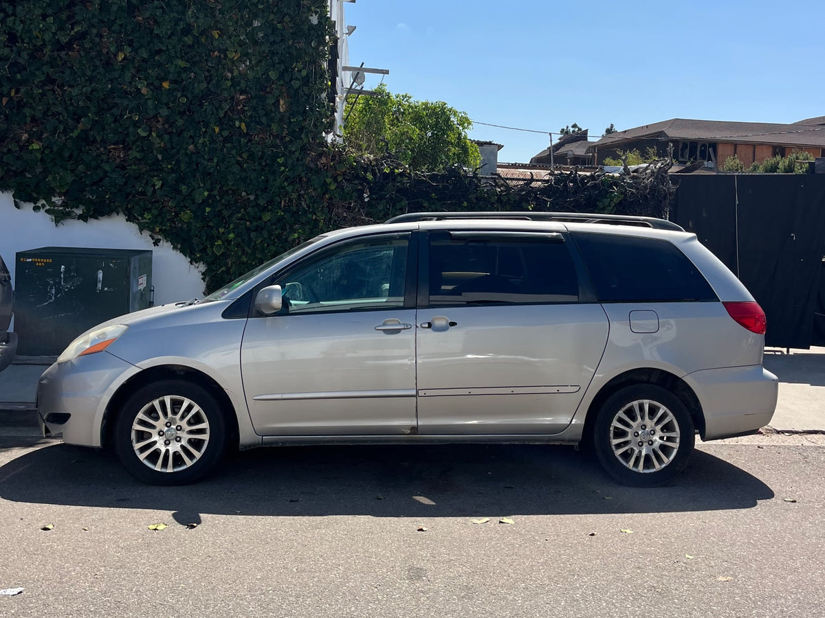 A silver minivan parked on a sunny street near an ivy-covered wall. Consider this vehicle as an alternative to an rv rental.|Rear view of a silver minivan with open tailgate