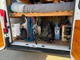 Explore the rear storage of this RV rental camper van, featuring a water heater, climbing gear, and power setup under the bed.