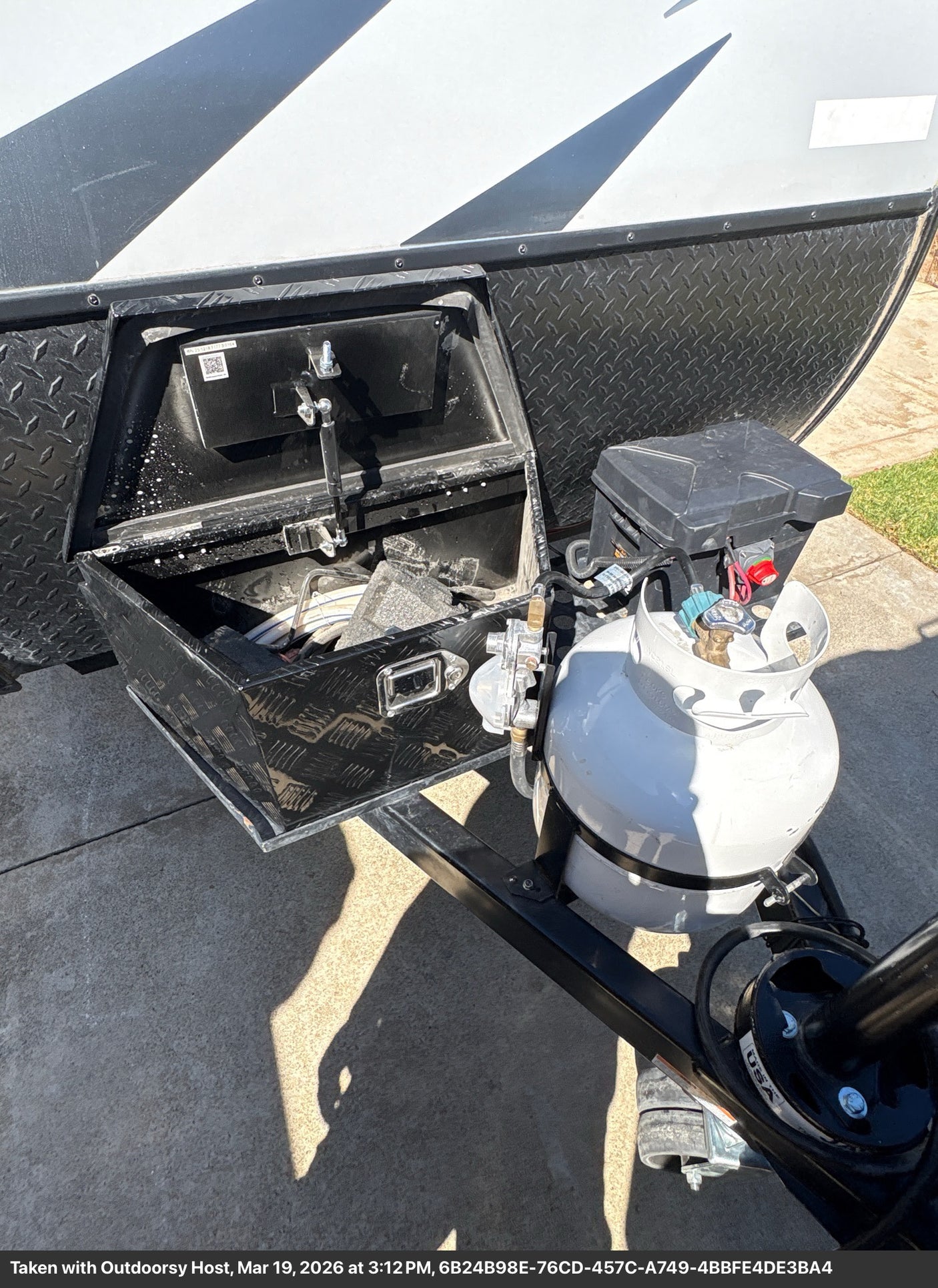 RV rental's front hitch area featuring an open storage box, propane tank, and battery for camping adventures.
