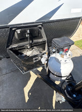 RV rental's front hitch area featuring an open storage box, propane tank, and battery for camping adventures.