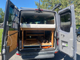 This RV rental camper van features a clever custom interior with a high bed, pull-out storage, & roof rack gear.