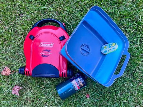 Portable Coleman stove, wash basin, and propane tank on grass. Essential gear for your next RV rental camping trip.