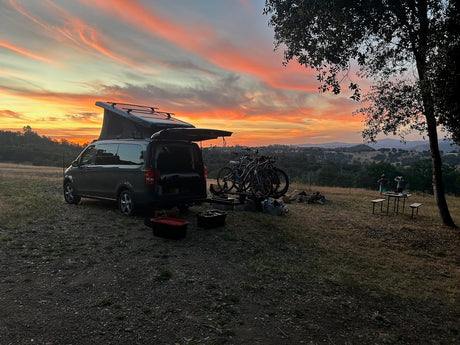 Gorgeous sunset over rolling hills from an RV rental camper van. Pop-top open, bikes ready for adventure, perfect for outdoor camping.