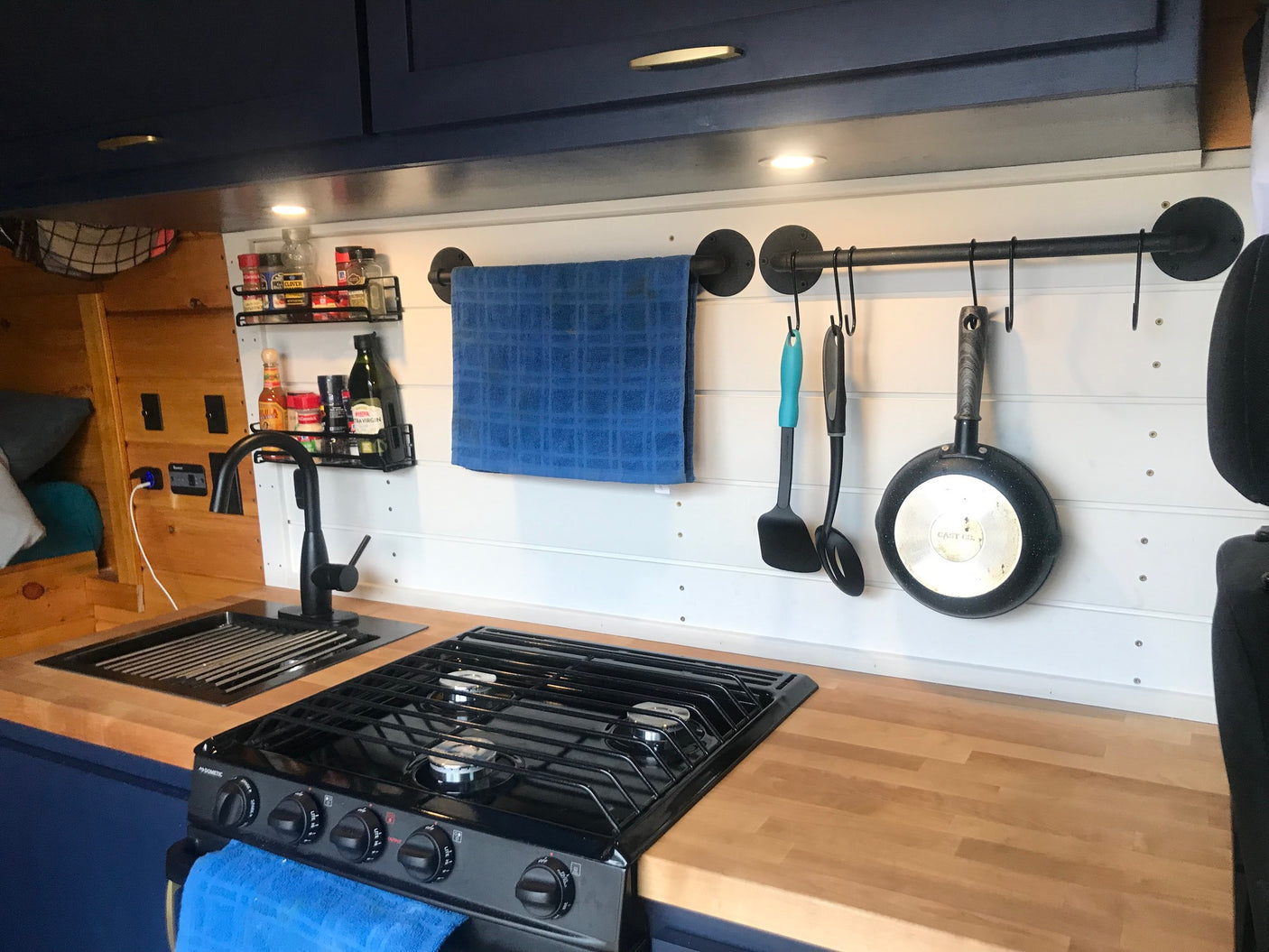 RV rental kitchen: wood counters, sink, stove, spice rack, and hanging rail with utensils & towel.