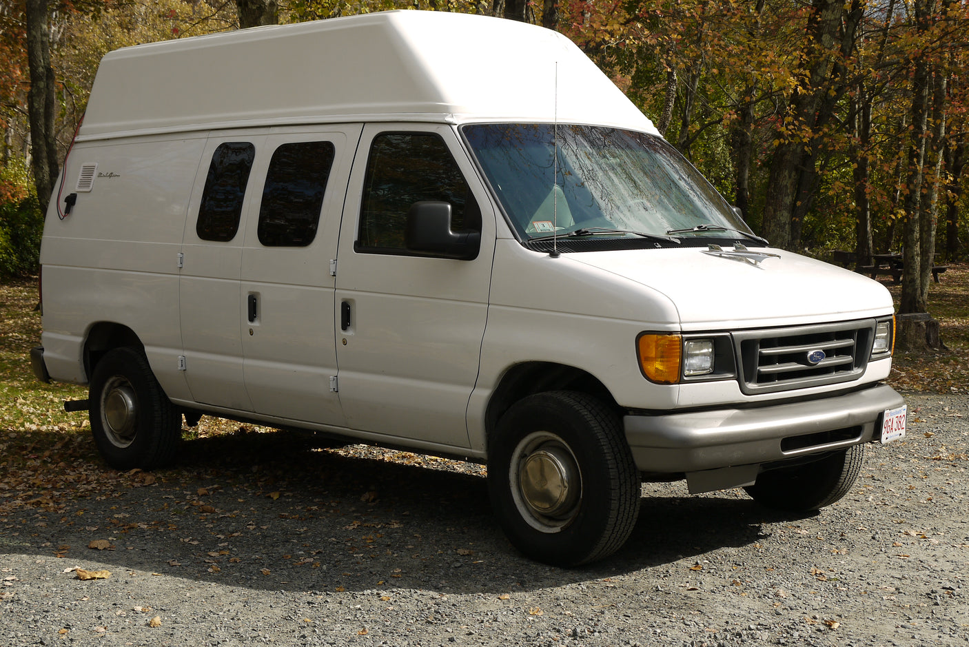 White high-top Ford RV rental van parked on gravel in autumn, ready for adventure.